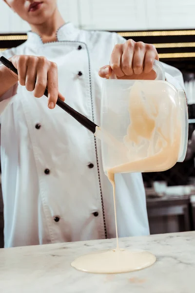 Cropped view of chocolatier pouring melted white chocolate on marble surface — Stock Photo