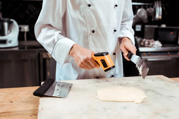 Vue recadrée du chocolatier mesurant la température du chocolat blanc fondu avec thermomètre de cuisson — Photo de stock