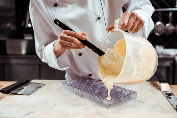 Vue recadrée du chocolatier versant du chocolat blanc fondu dans un plateau de glace — Photo de stock