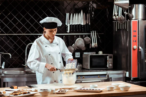 Chocolatier pouring melted white chocolate into bowl while holding cake scraper — Stock Photo