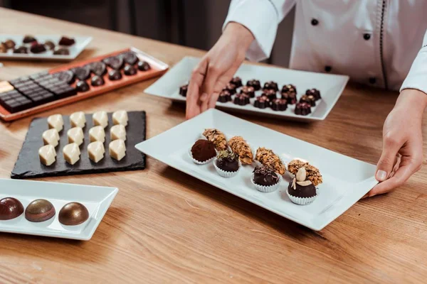 Cropped view of chocolatier touching plate with tasty and fresh made chocolate balls — Stock Photo