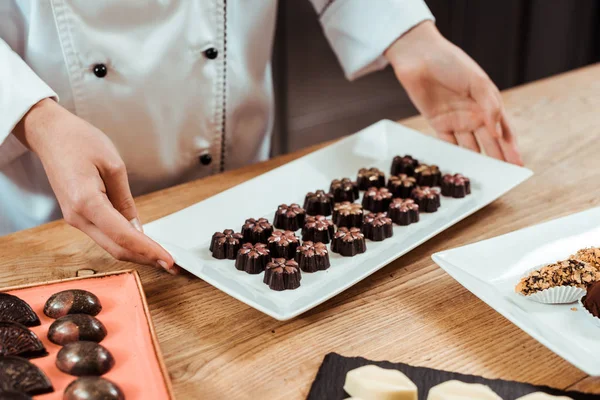 Cropped view of chocolatier touching plate with tasty chocolate balls — Stock Photo