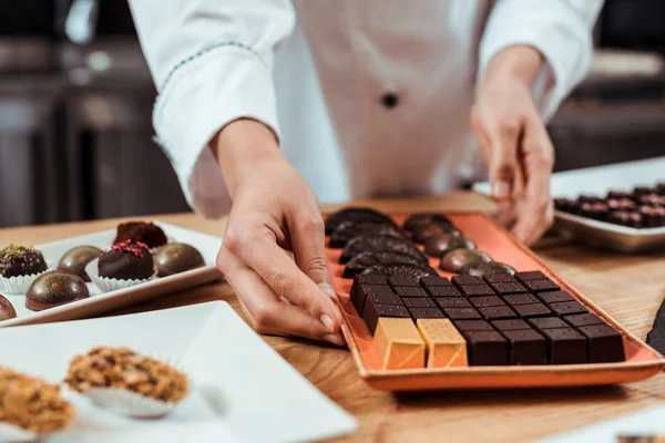 Vista recortada de chocolate tocando plato con sabrosos caramelos de chocolate cerca de bolas de chocolate - foto de stock