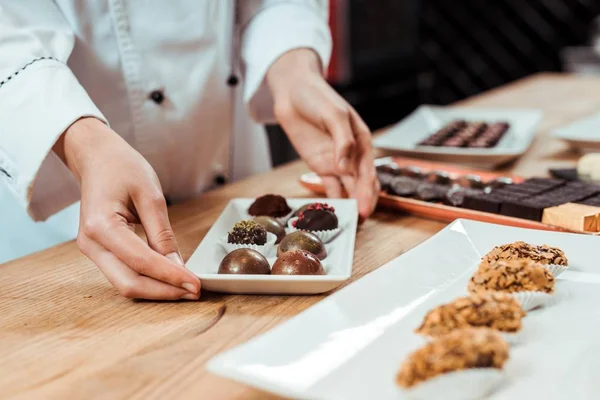 Cropped view of chocolatier touching plate with chocolate candies — Stock Photo