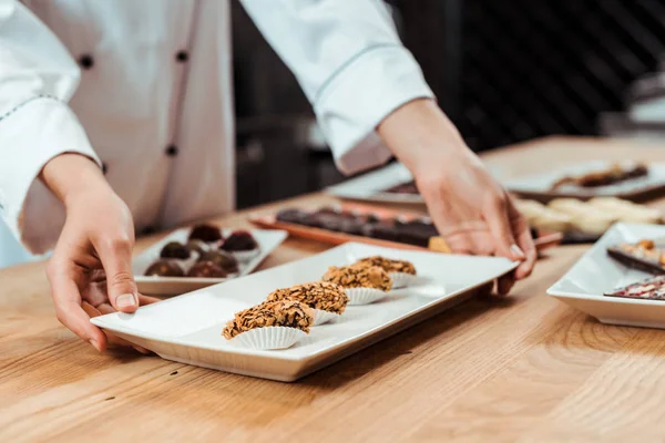 Cropped view of woman touching plate with chocolate candies — Stock Photo