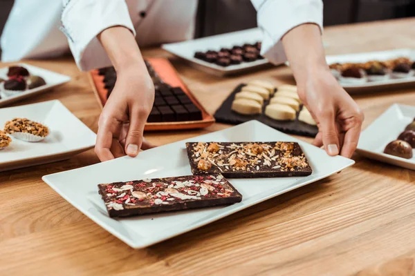 Cropped view of woman touching plate with fresh made chocolate bars — Stock Photo