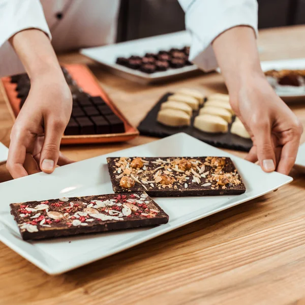 Vue recadrée de femme touchant plaque avec des barres de chocolat fraîches préparées — Photo de stock