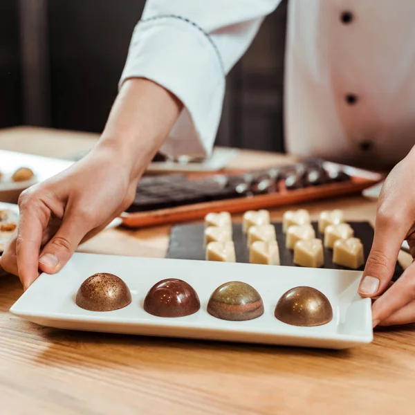 Cropped view of chocolatier touching plate with sweet chocolate candies — Stock Photo