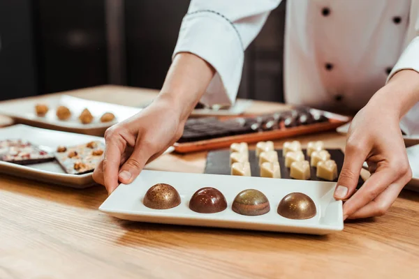 Cropped view of chocolatier touching plate with sweet and fresh chocolate candies — Stock Photo