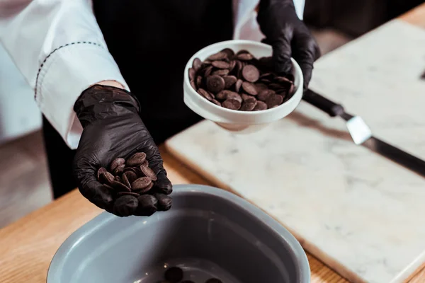 Cropped view of chocolatier holing dark chocolate chips in hand — Stock Photo