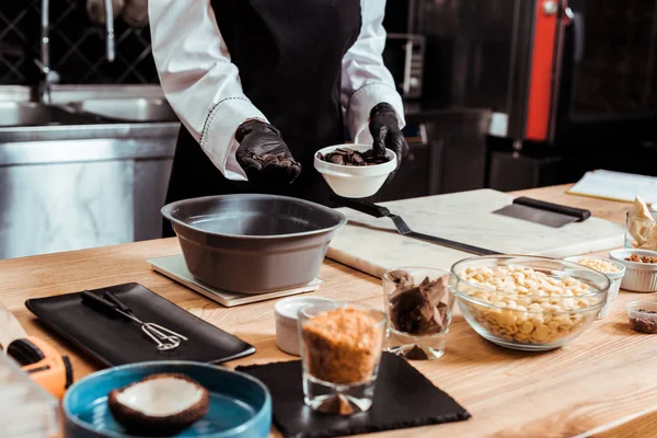 Ausgeschnittene Ansicht eines Chocolatiers, der Schokoladenchips in Schüssel auf Küchenwaage gibt — Stockfoto