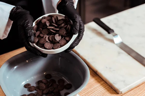 Cropped view of chocolatier holding chocolate chips into bowl — Stock Photo