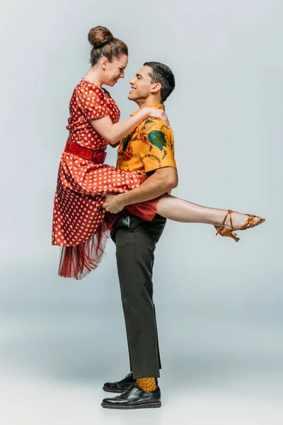 Vue latérale du danseur tenant fille gaie tout en dansant boogie-woogie sur fond gris — Stock Photo