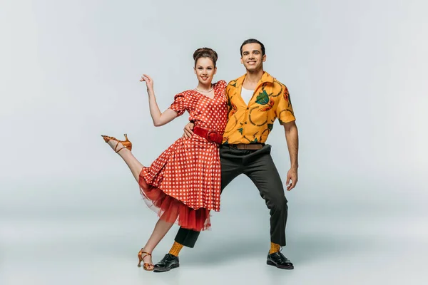 Jeunes danseurs souriant à la caméra tout en dansant boogie-woogie sur fond gris — Photo de stock