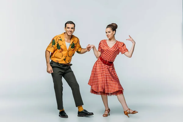 Smiling dancers looking at camera while dancing boogie-woogie on grey background — Stock Photo