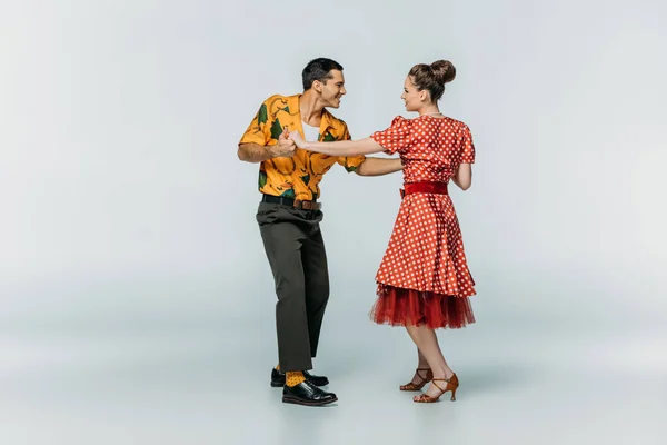 Bailarinos sorridentes olhando um para o outro enquanto dançam boogie-woogie em fundo cinza — Fotografia de Stock