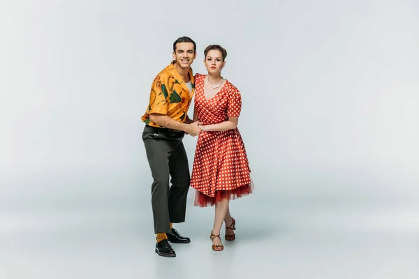 Smiling dancers looking at camera while dancing boogie-woogie on grey background — Stock Photo