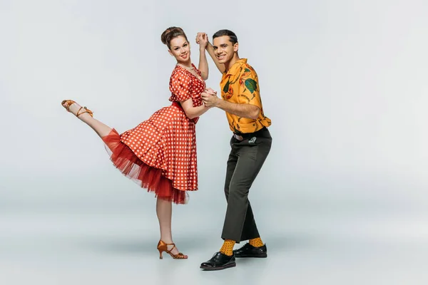 Bailarines sonrientes tomados de la mano mientras bailan boogie-woogie sobre fondo gris - foto de stock