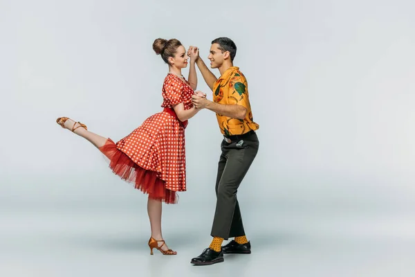 Cheerful dancers holding hands while dancing boogie-woogie on grey background — Stock Photo