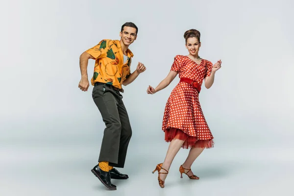 Cheerful dancers looking at camera while dancing boogie-woogie on grey background — Stock Photo