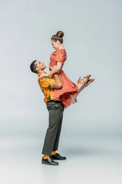 Вид збоку красивого танцюриста, який тримає партнера під час танцю бугі-вугілля на сірому фоні — стокове фото