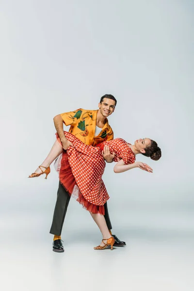 Sonriente bailarina de apoyo pareja mientras baila boogie-woogie sobre fondo gris - foto de stock