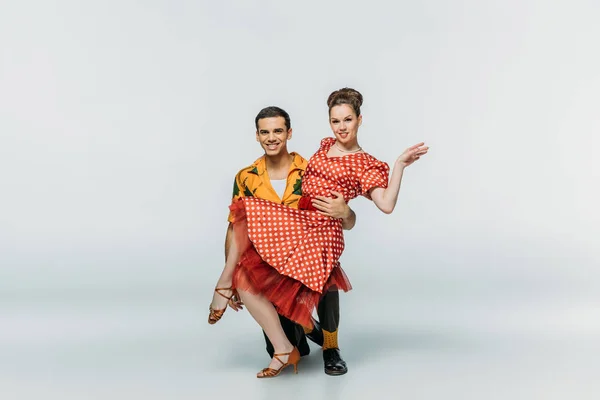 Усміхнений танцюрист, що стоїть на коліні і підтримує партнера, танцюючи бугі-вугілля на сірому фоні — стокове фото