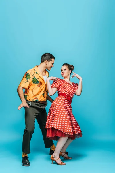 Bailarines alegres mirándose mientras bailan boogie-woogie sobre fondo azul - foto de stock