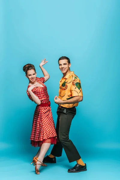 Danseurs joyeux regardant la caméra tout en dansant boogie-woogie sur fond bleu — Photo de stock