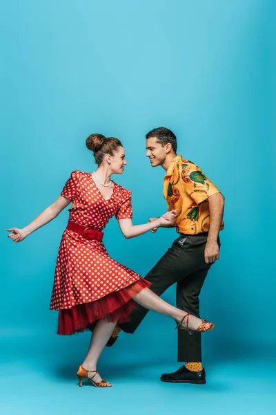 Lächelnde Tänzer, die sich beim Tanzen des Boogie-Woogie auf blauem Hintergrund anschauen — Stockfoto