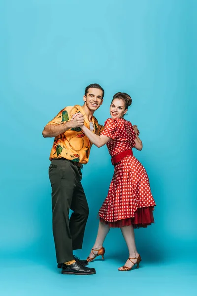 Stylish dancers holding hands while dancing boogie-woogie on blue background — Stock Photo