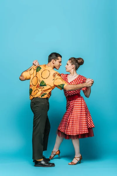Stylish dancers holding hands while dancing boogie-woogie on blue background — Stock Photo