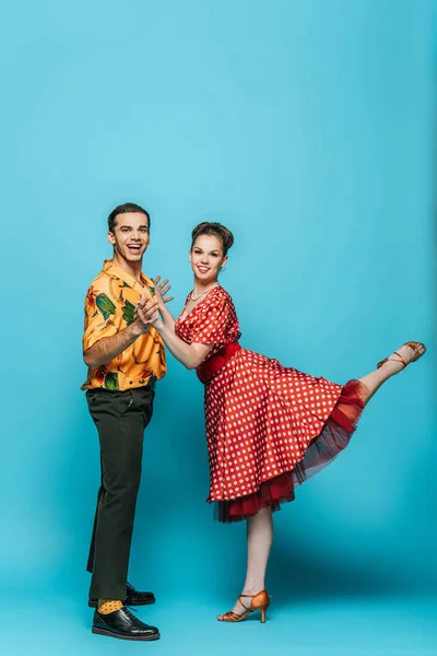 Happy dancers looking at camera while dancing boogie-woogie on blue background — Stock Photo