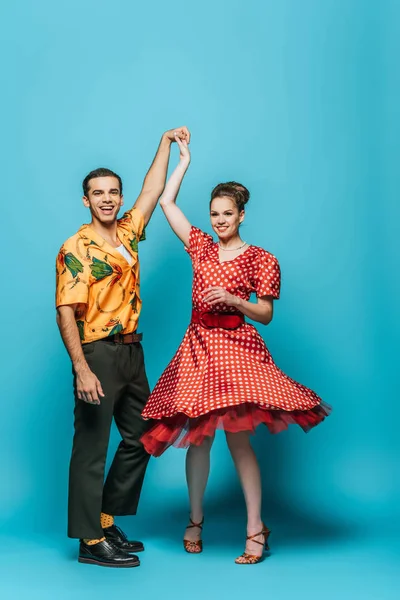 Happy dancers holding hands while dancing boogie-woogie on blue background — Stock Photo
