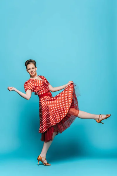 Pretty, smiling dancer looking at camera while dancing boogie-woogie on blue background — Stock Photo