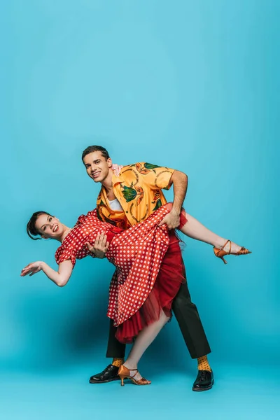 Homem bonito apoiando mulher elegante enquanto dança boogie-woogie no fundo azul — Fotografia de Stock