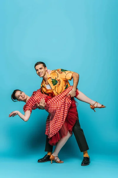 Bel homme soutenant femme élégante tout en dansant boogie-woogie sur fond bleu — Photo de stock