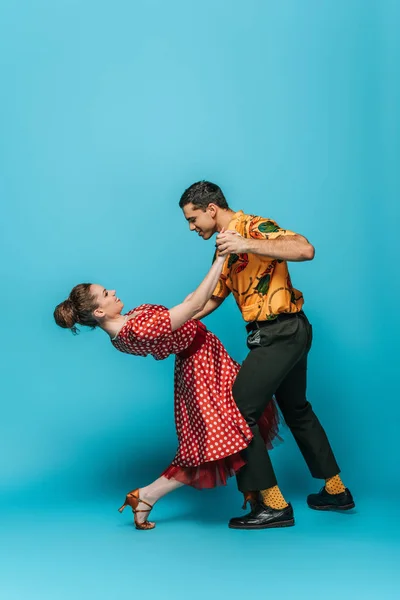 Side view of young dancers holding hands while dancing boogie-woogie on blue background — Stock Photo