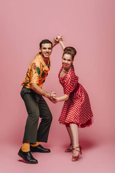 Bailarines sonrientes mirando a la cámara mientras bailan boogie-woogie sobre fondo rosa - foto de stock