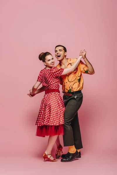 Stylish dancers holding hands while dancing boogie-woogie on pink background — Stock Photo