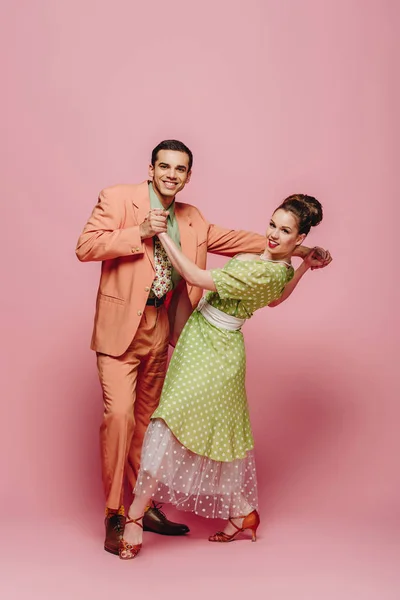 Bailarines felices mirando a la cámara mientras bailan boogie-woogie sobre fondo rosa - foto de stock