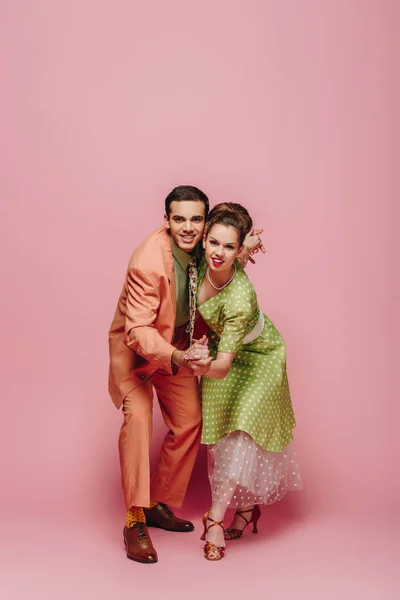 Cheerful dancers holding hands while dancing boogie-woogie on pink background — Stock Photo