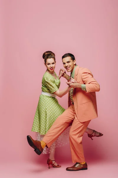 Young dancers holding hands while dancing boogie-woogie on pink background — Stock Photo