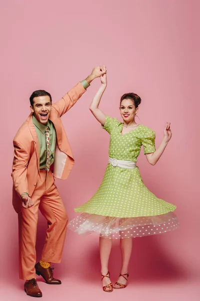 Cheerful dancers holding hands while dancing boogie-woogie on pink background — Stock Photo