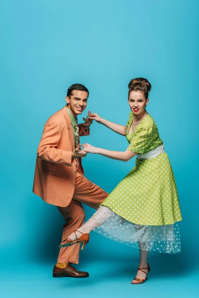 Danseurs joyeux regardant la caméra tout en dansant boogie-woogie sur fond bleu — Photo de stock