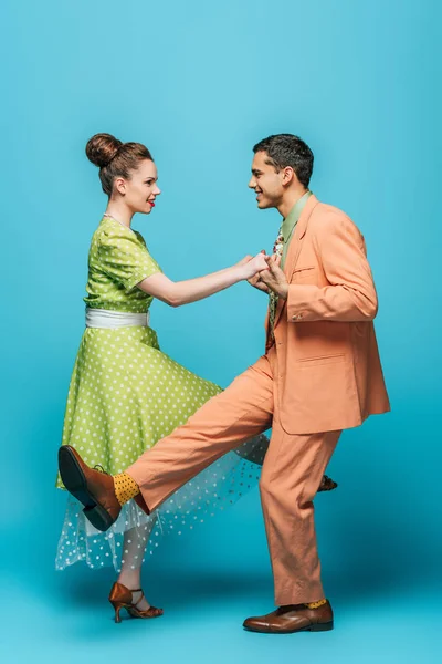 Vue latérale de danseurs élégants tenant la main tout en dansant boogie-woogie sur fond bleu — Photo de stock