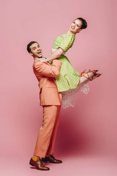 Elegante bailarina sosteniendo chica mientras baila boogie-woogie sobre fondo rosa - foto de stock