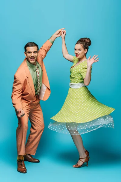 Bailarines elegantes tomados de la mano mientras bailan boogie-woogie sobre fondo azul - foto de stock