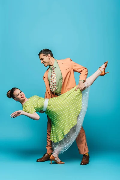 Stylish dancer supporting girl while dancing boogie-woogie on blue background — Stock Photo