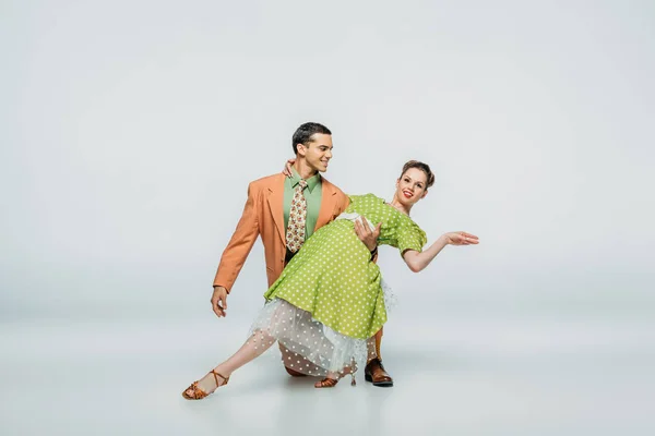 Guapo bailarín de pie en la rodilla y pareja de apoyo mientras baila boogie-woogie sobre fondo gris - foto de stock